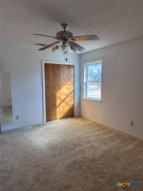 unfurnished bedroom featuring visible vents, carpet floors, a textured ceiling, and a ceiling fan