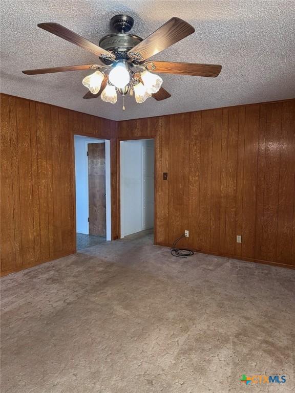 unfurnished room with wooden walls, carpet flooring, and a textured ceiling