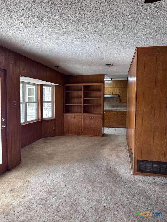 unfurnished room featuring a textured ceiling, visible vents, wood walls, and light carpet