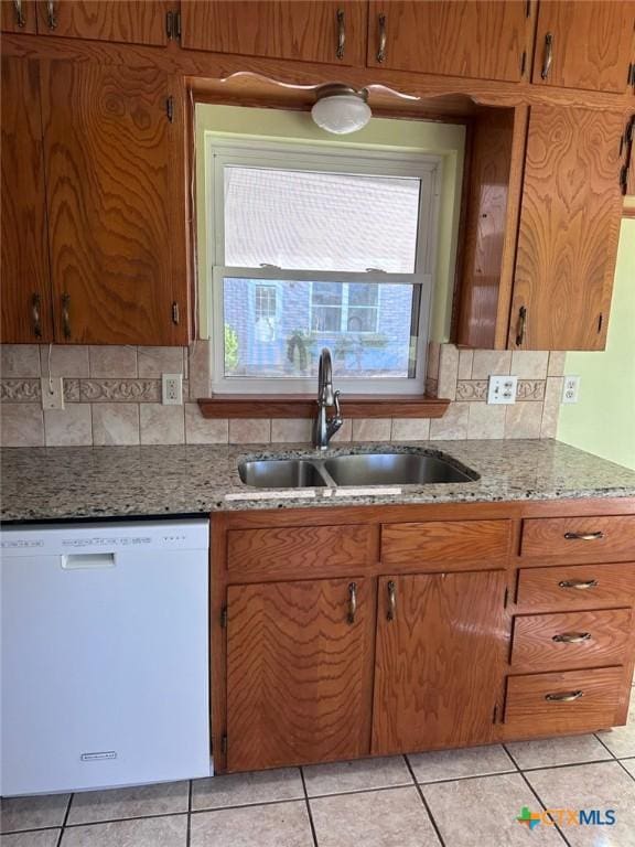 kitchen with light stone countertops, white dishwasher, a sink, tasteful backsplash, and brown cabinets