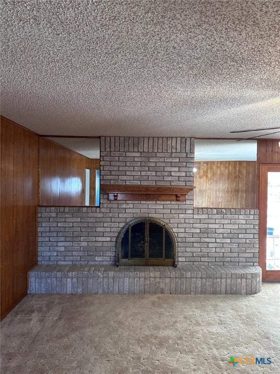 unfurnished living room with carpet flooring, wood walls, a brick fireplace, and a textured ceiling