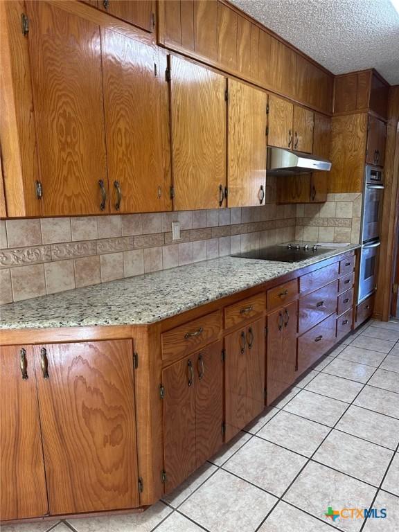 kitchen with under cabinet range hood, stainless steel double oven, light tile patterned flooring, and a textured ceiling