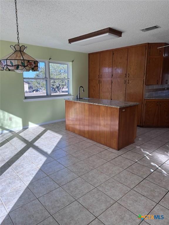 kitchen with visible vents, brown cabinetry, hanging light fixtures, a textured ceiling, and a sink