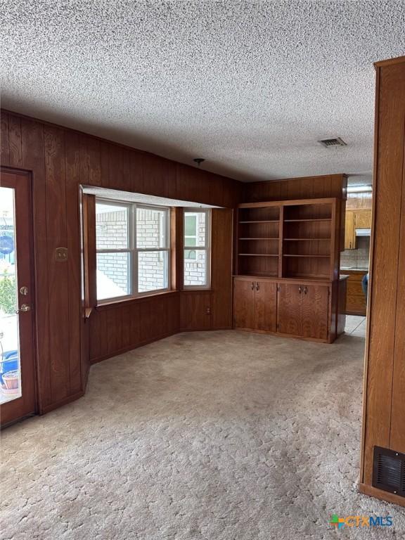 unfurnished living room featuring visible vents, carpet, and wood walls