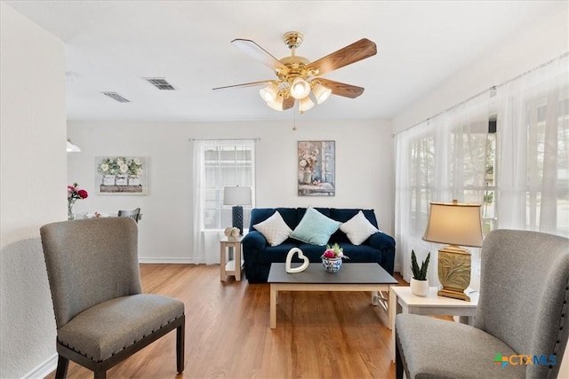 living area with light wood-style floors, ceiling fan, visible vents, and baseboards