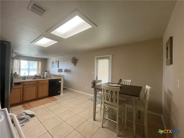 kitchen featuring light tile patterned floors, visible vents, freestanding refrigerator, dishwasher, and brown cabinets