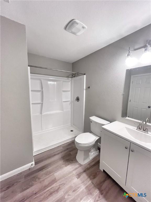 bathroom with visible vents, toilet, wood finished floors, vanity, and a shower