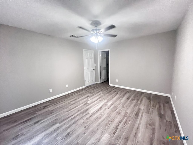 empty room featuring ceiling fan, wood finished floors, visible vents, and baseboards