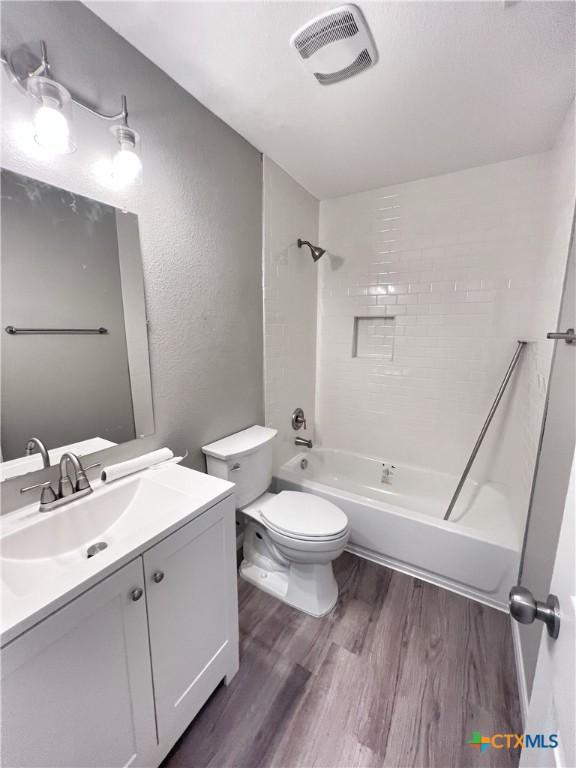 bathroom featuring visible vents, toilet, vanity, wood finished floors, and washtub / shower combination