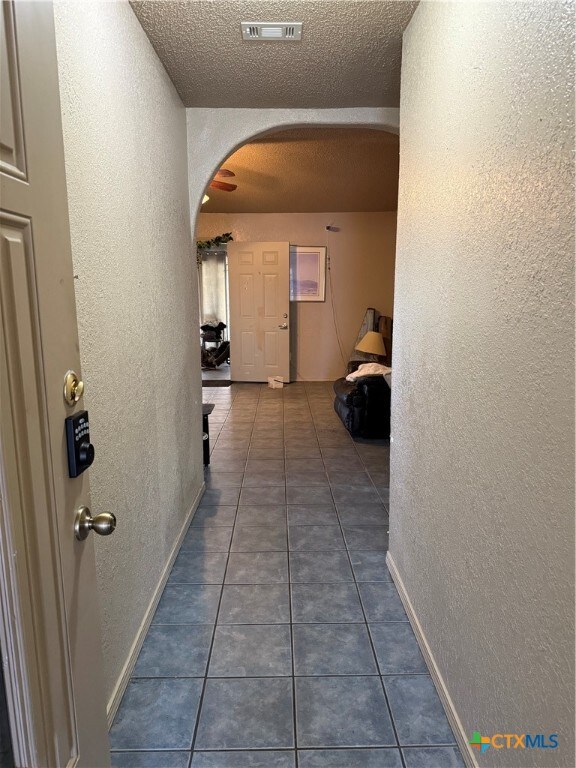 hallway featuring dark tile patterned floors and a textured ceiling