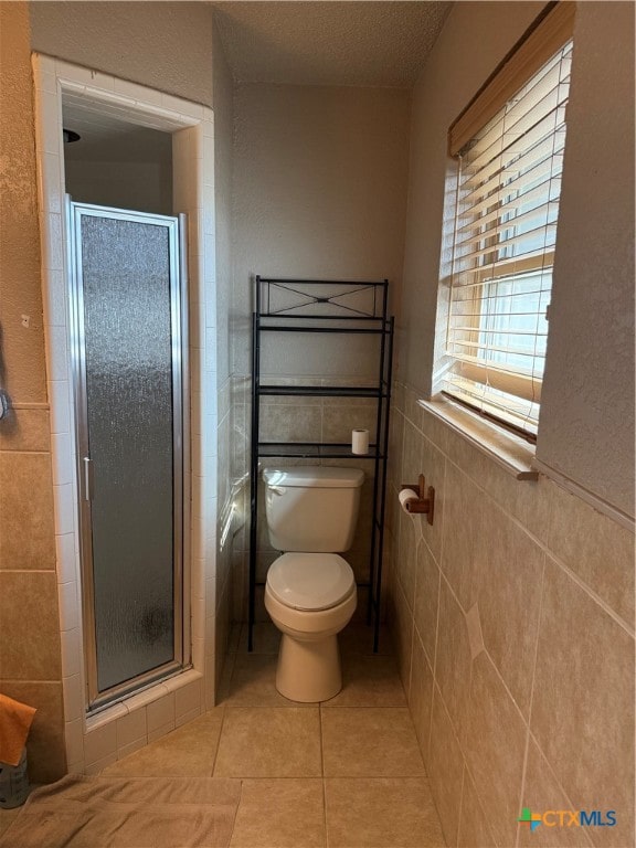 bathroom featuring tile patterned flooring, a textured ceiling, toilet, a shower with door, and tile walls