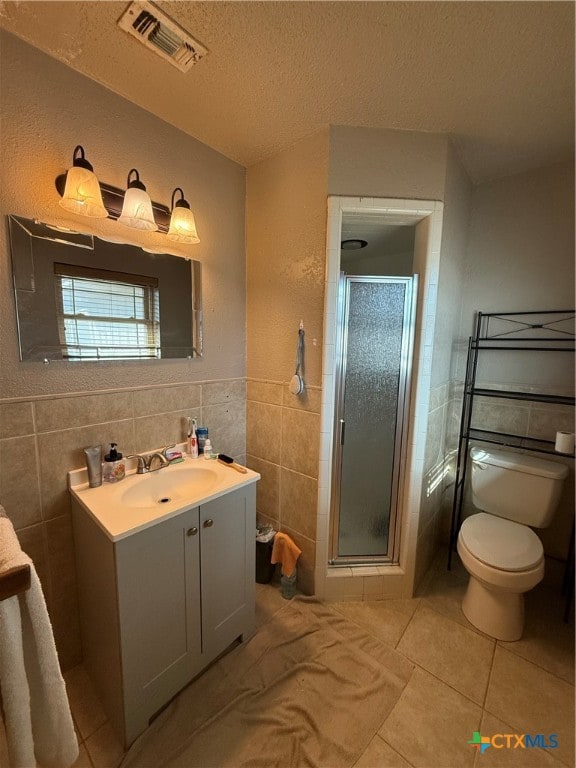 bathroom featuring vanity, a textured ceiling, tile walls, tile patterned flooring, and a shower with shower door