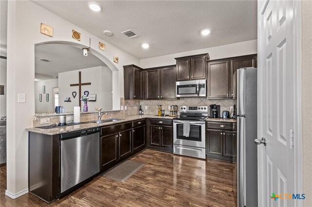 853 Hobby Rd, Copperas Cove, TX 76522 - kitchen with stainless steel appliances, dark wood-type flooring, dark brown cabinetry, arched walkways, and light stone counters