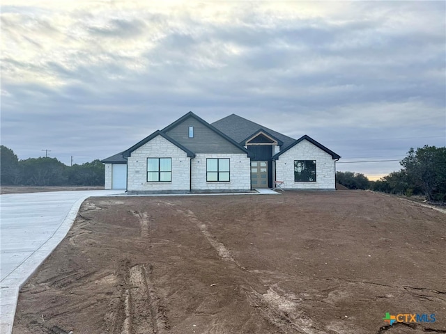 modern farmhouse with an attached garage, stone siding, and concrete driveway