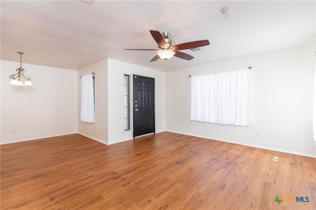 empty room featuring ceiling fan with notable chandelier and hardwood / wood-style flooring