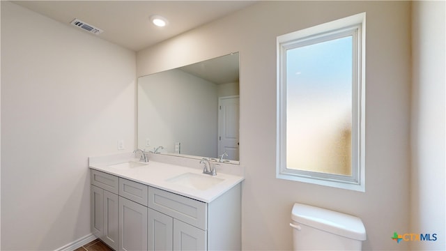 bathroom featuring double vanity, visible vents, toilet, and a sink