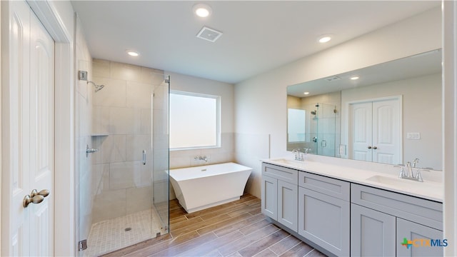 bathroom featuring double vanity, tile walls, visible vents, wood finished floors, and a shower stall
