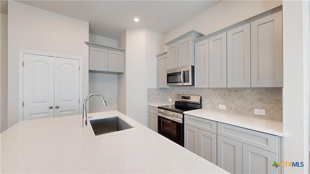 kitchen with recessed lighting, backsplash, a sink, gray cabinetry, and appliances with stainless steel finishes