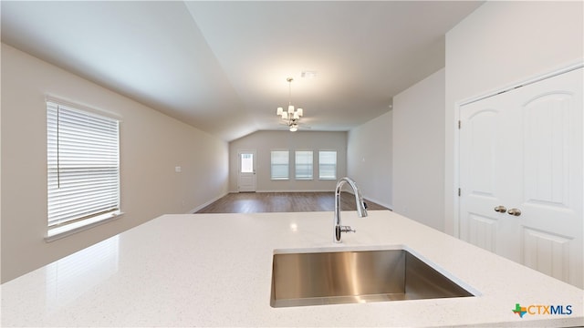 kitchen with lofted ceiling, light stone counters, a sink, decorative light fixtures, and open floor plan