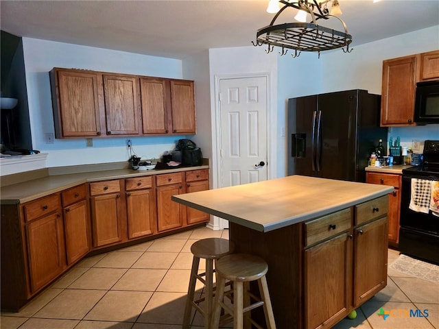 kitchen with light tile patterned flooring, black appliances, a breakfast bar area, an inviting chandelier, and a kitchen island