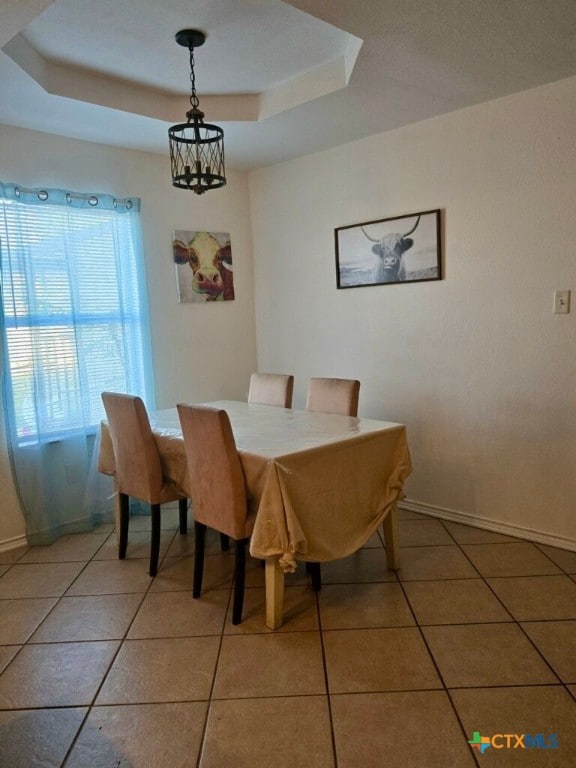 dining space featuring tile patterned flooring, a raised ceiling, and an inviting chandelier