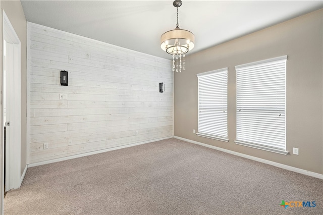 carpeted spare room featuring wood walls and a notable chandelier