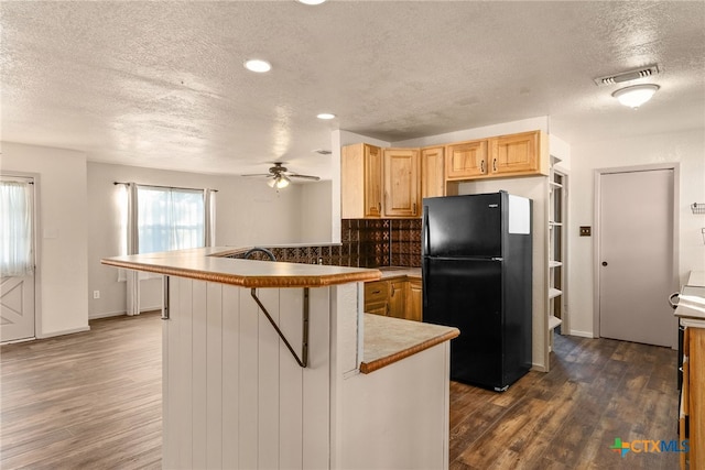 kitchen featuring black fridge, dark hardwood / wood-style floors, a kitchen breakfast bar, and kitchen peninsula