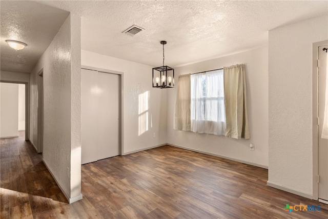 unfurnished dining area with dark hardwood / wood-style flooring, a textured ceiling, and an inviting chandelier