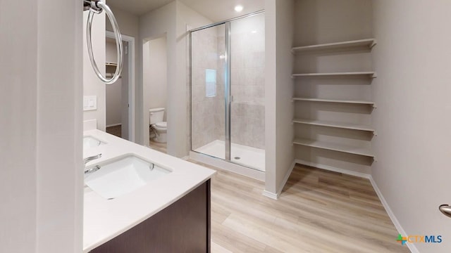 bathroom featuring toilet, double vanity, a stall shower, wood finished floors, and a sink