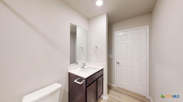 half bath with toilet, vanity, baseboards, and wood finished floors