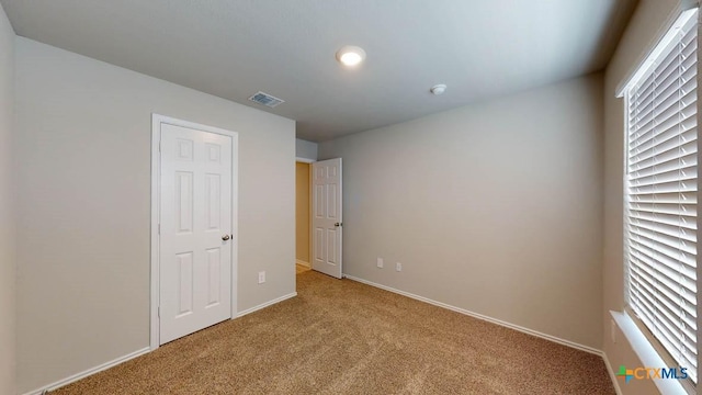 unfurnished bedroom featuring visible vents, multiple windows, and light colored carpet