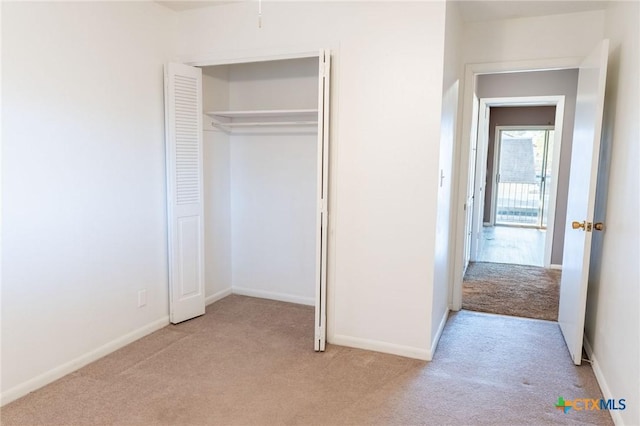 unfurnished bedroom with a closet, light colored carpet, and baseboards