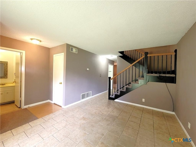 spare room with stairway, baseboards, visible vents, and a textured ceiling