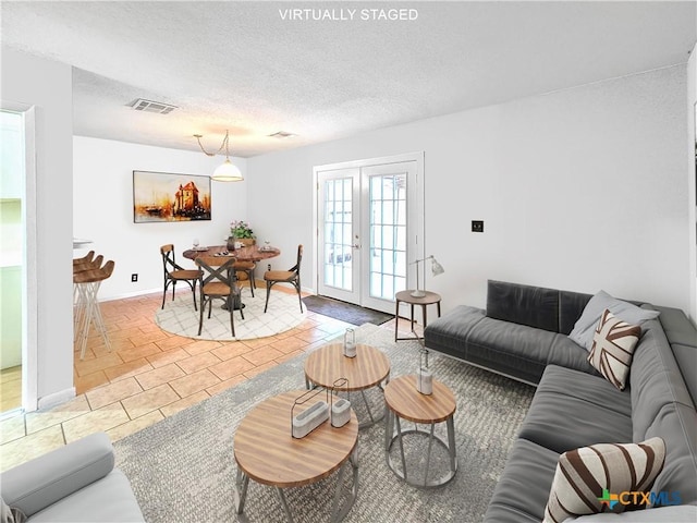 living room with a textured ceiling, light tile patterned floors, visible vents, baseboards, and french doors