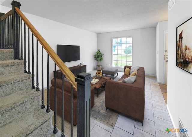 living room featuring light tile patterned floors, baseboards, stairway, and a textured ceiling