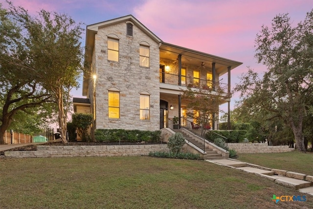 view of front of home with ceiling fan, a balcony, and a yard