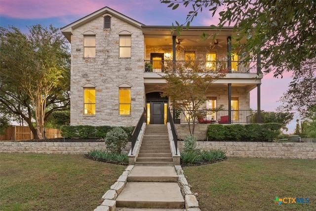 view of front of property with a lawn, ceiling fan, a balcony, and covered porch