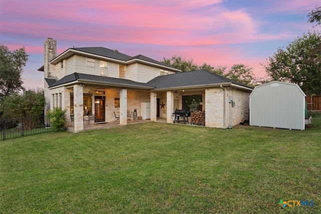 back house at dusk with a patio area, a yard, and a storage unit