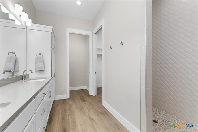 bathroom with baseboards, double vanity, tiled shower, wood finished floors, and a sink