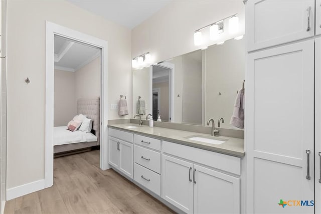 ensuite bathroom featuring double vanity, wood finished floors, baseboards, and a sink