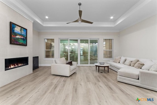 living area with a raised ceiling, a fireplace, and light wood finished floors