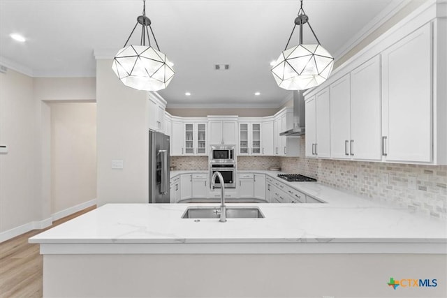 kitchen with sink, white cabinetry, hanging light fixtures, appliances with stainless steel finishes, and wall chimney range hood