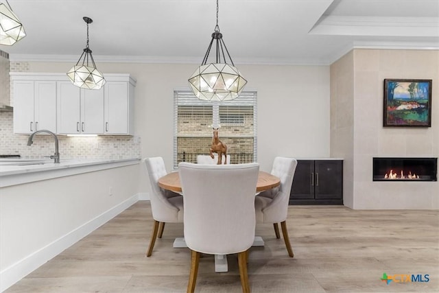 dining space with light wood finished floors, a tile fireplace, crown molding, and baseboards