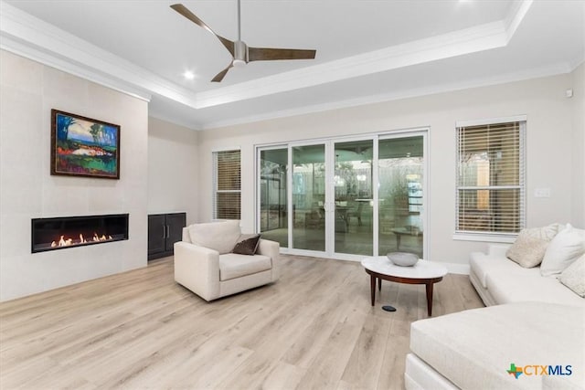 interior space featuring a tiled fireplace, ornamental molding, ceiling fan, a raised ceiling, and light hardwood / wood-style flooring