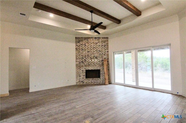 unfurnished living room with beam ceiling, a towering ceiling, hardwood / wood-style flooring, ceiling fan, and a fireplace