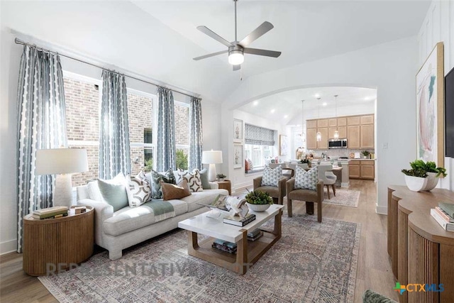 living room with arched walkways, lofted ceiling, a ceiling fan, baseboards, and light wood-style floors