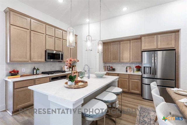 kitchen featuring decorative light fixtures, stainless steel appliances, a kitchen breakfast bar, light countertops, and a center island with sink