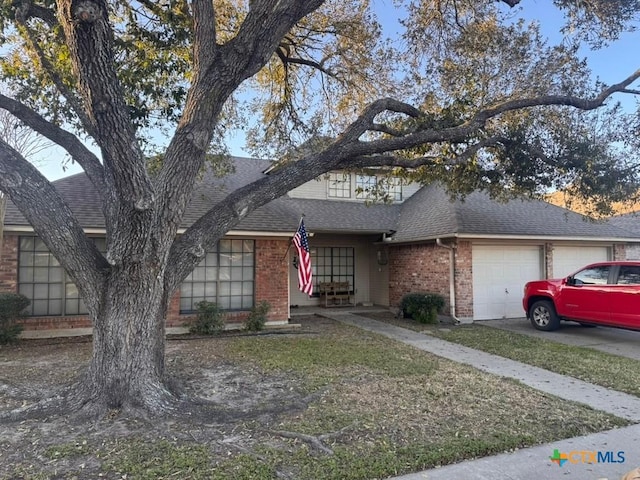 view of front facade featuring a front yard, driveway, a shingled roof, a garage, and brick siding