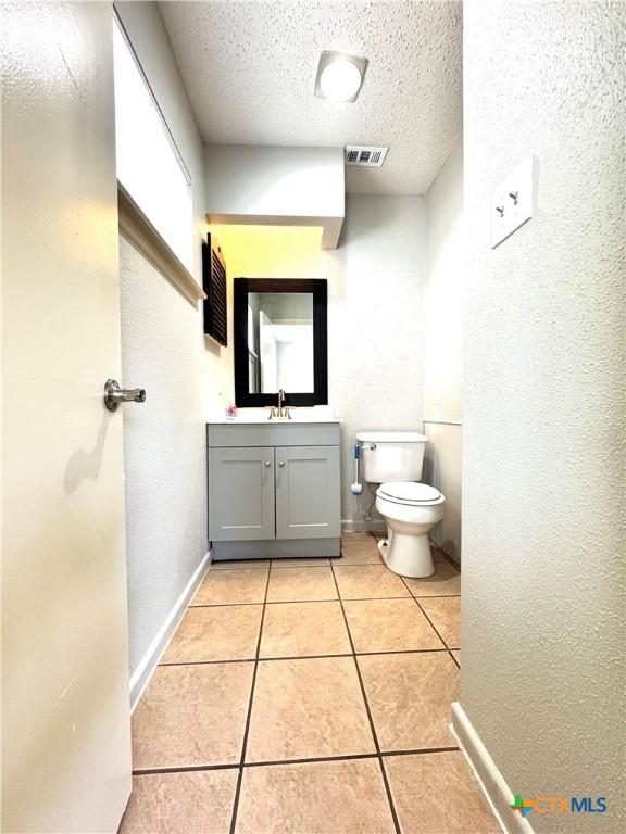 6430 Ridge Village Dr, San Antonio, TX 78233 - half bath with a textured ceiling, toilet, tile patterned floors, vanity, and baseboards