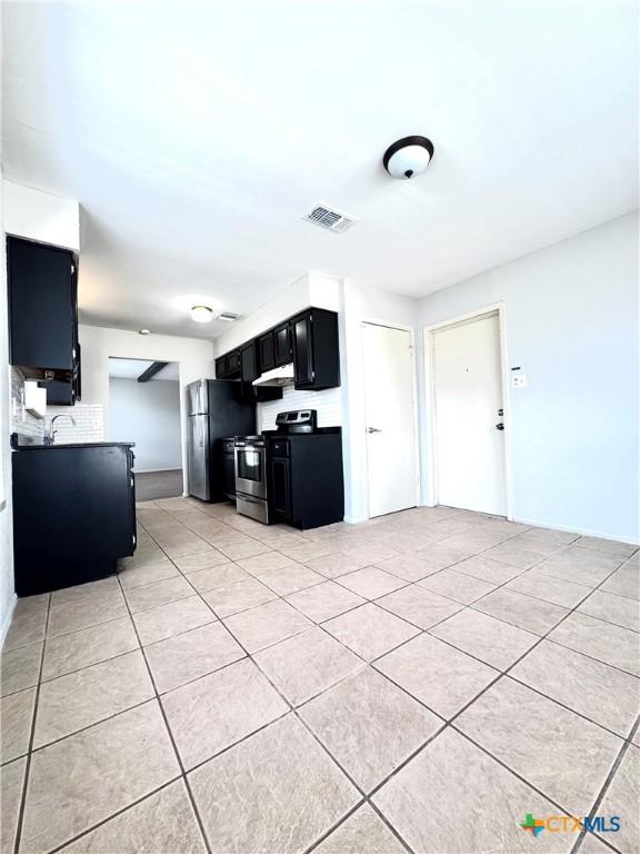 6430 Ridge Village Dr, San Antonio, TX 78233 - kitchen with electric stove, dark cabinetry, freestanding refrigerator, under cabinet range hood, and light tile patterned flooring